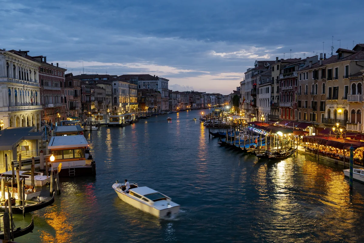 The Grand Canal in Venice at dusk, lined with lit historic buildings and boats
